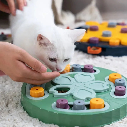PataFeliz green interactive puzzle feeder for cats with multiple compartments and colorful caps, a white cat is eating from a human hand.